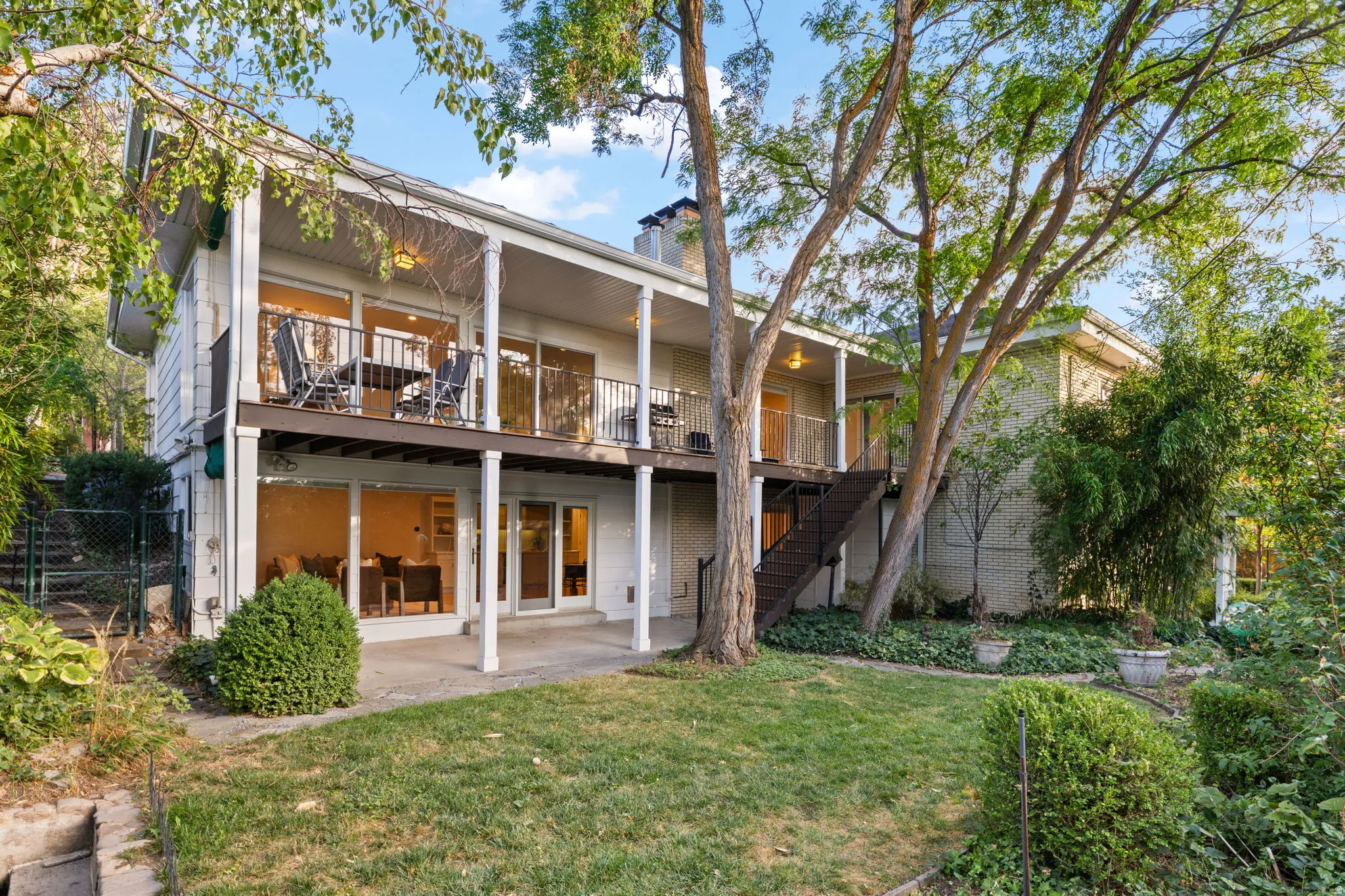 Two-story exterior with multiple balconies, a ground-level patio, and extensive natural landscaping