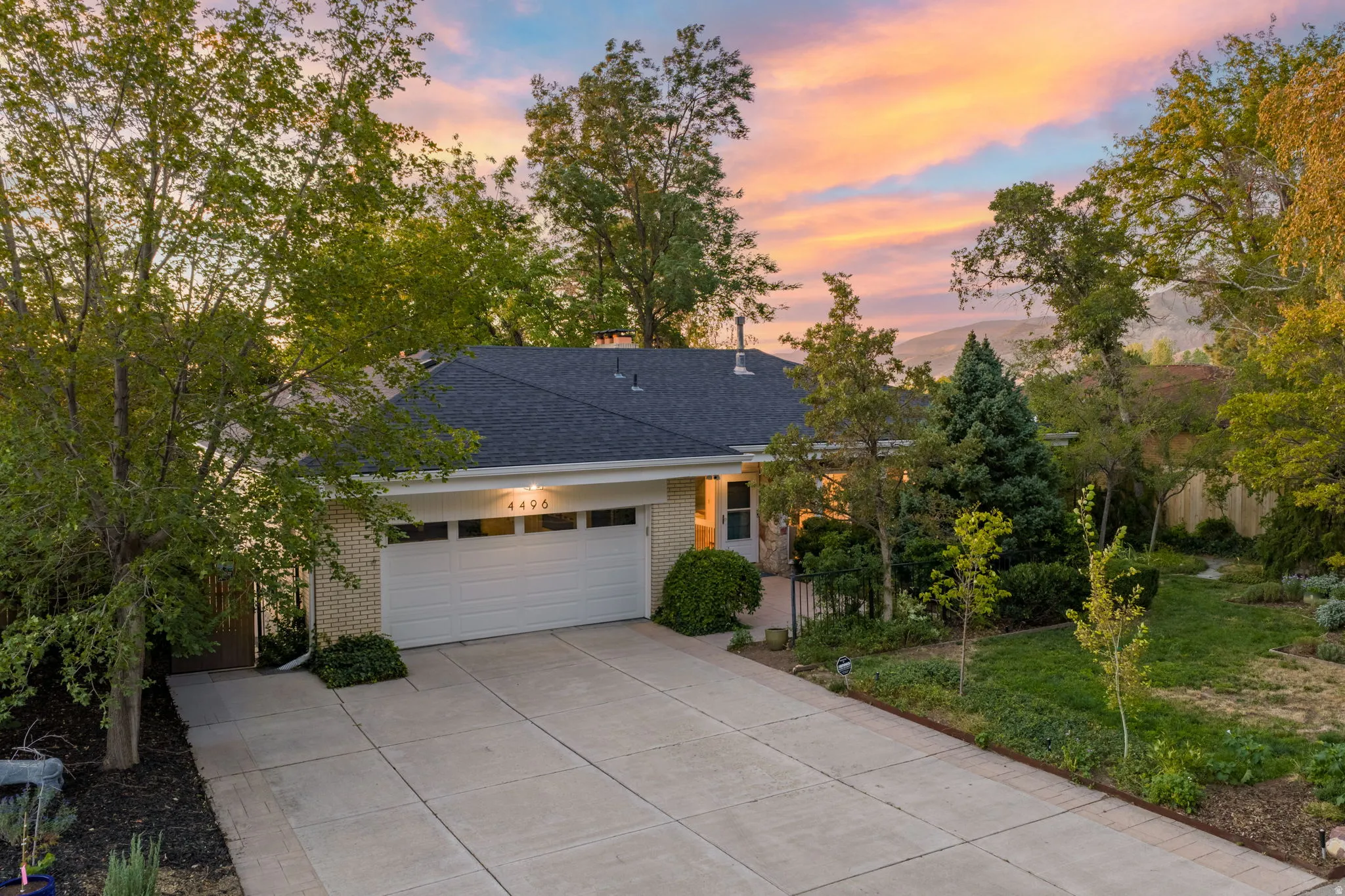 Brick exterior with a dark-shingled roof, featuring an attached garage with a panel door, a concrete driveway, and mature landscaping
