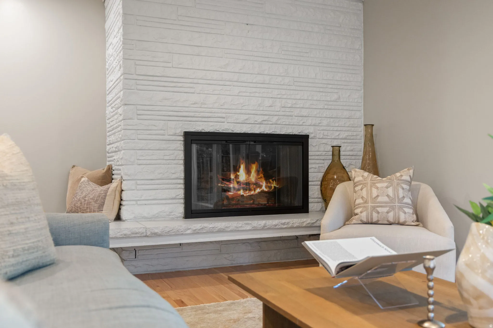 White stacked stone fireplace with a black framed firebox and stone hearth, complemented by light-colored walls and wood-finish flooring