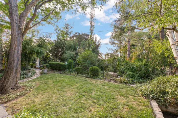 Grassy outdoor area featuring mature trees, a stone pathway, and a white garden arbor