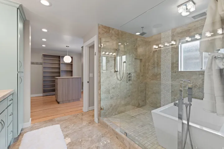 Full walk-in shower with glass enclosure, freestanding soaking tub, recessed lighting, and built-in closet shelving with a central island