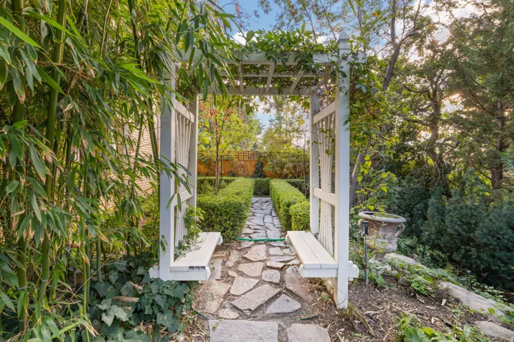 Landscaped pathway with flagstone pavers, a white pergola, and manicured hedges