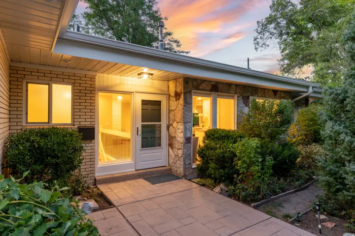 Stone and brick exterior with a covered entry, exterior lighting, and mature landscaping