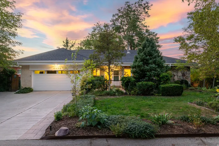 Brick exterior with an attached garage, featuring a concrete driveway, mature trees, and established landscaping