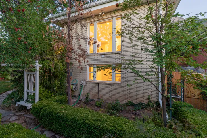 Brick exterior with white window trim, mature landscaping, and a flagstone pathway