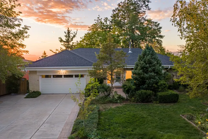 Brick facade with stone accents, attached garage, concrete driveway, lush landscaping, and mature trees