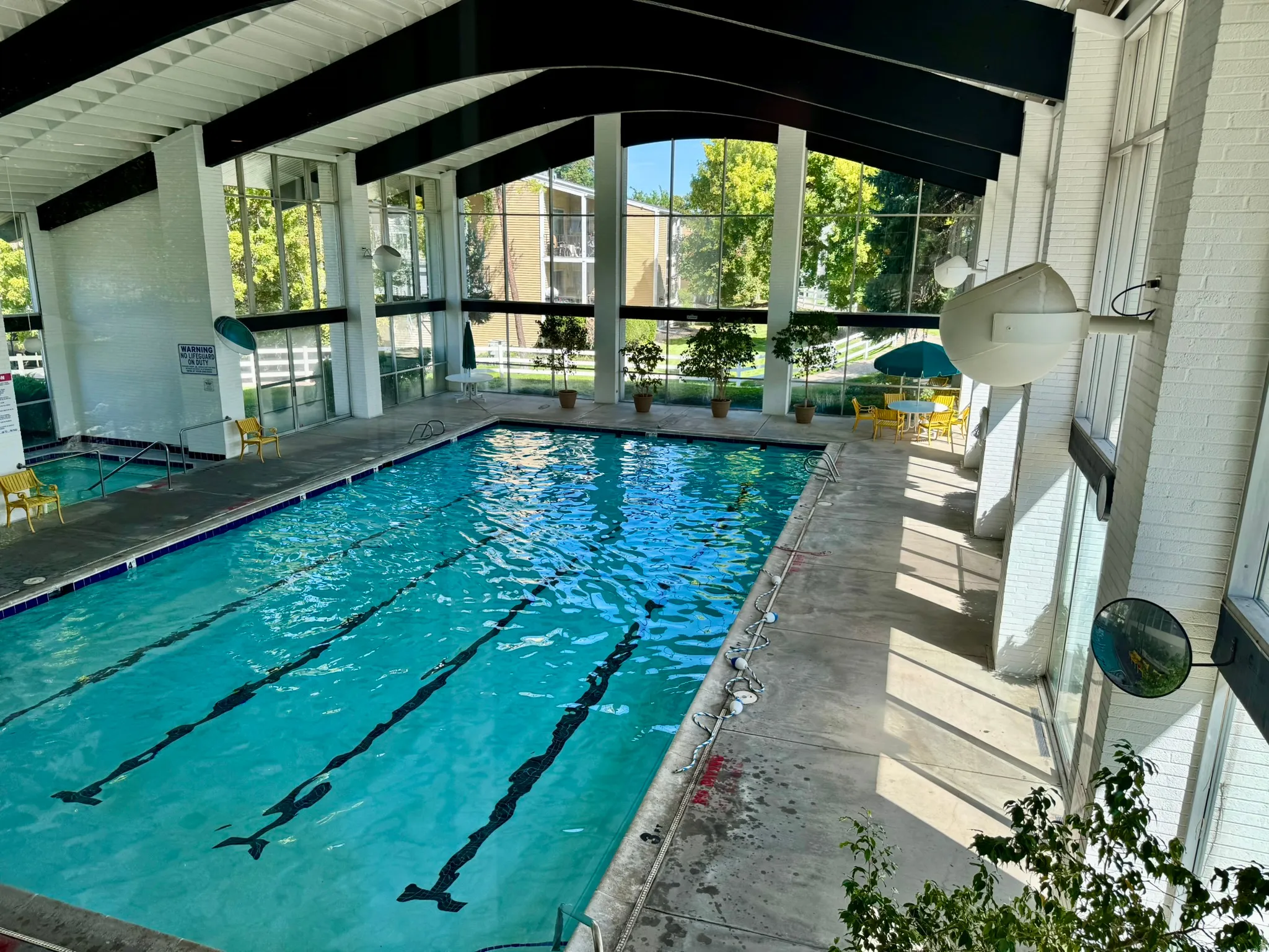 Indoor swimming pool with lane markers, integrated hot tub, abundant natural light, and exposed structural beams