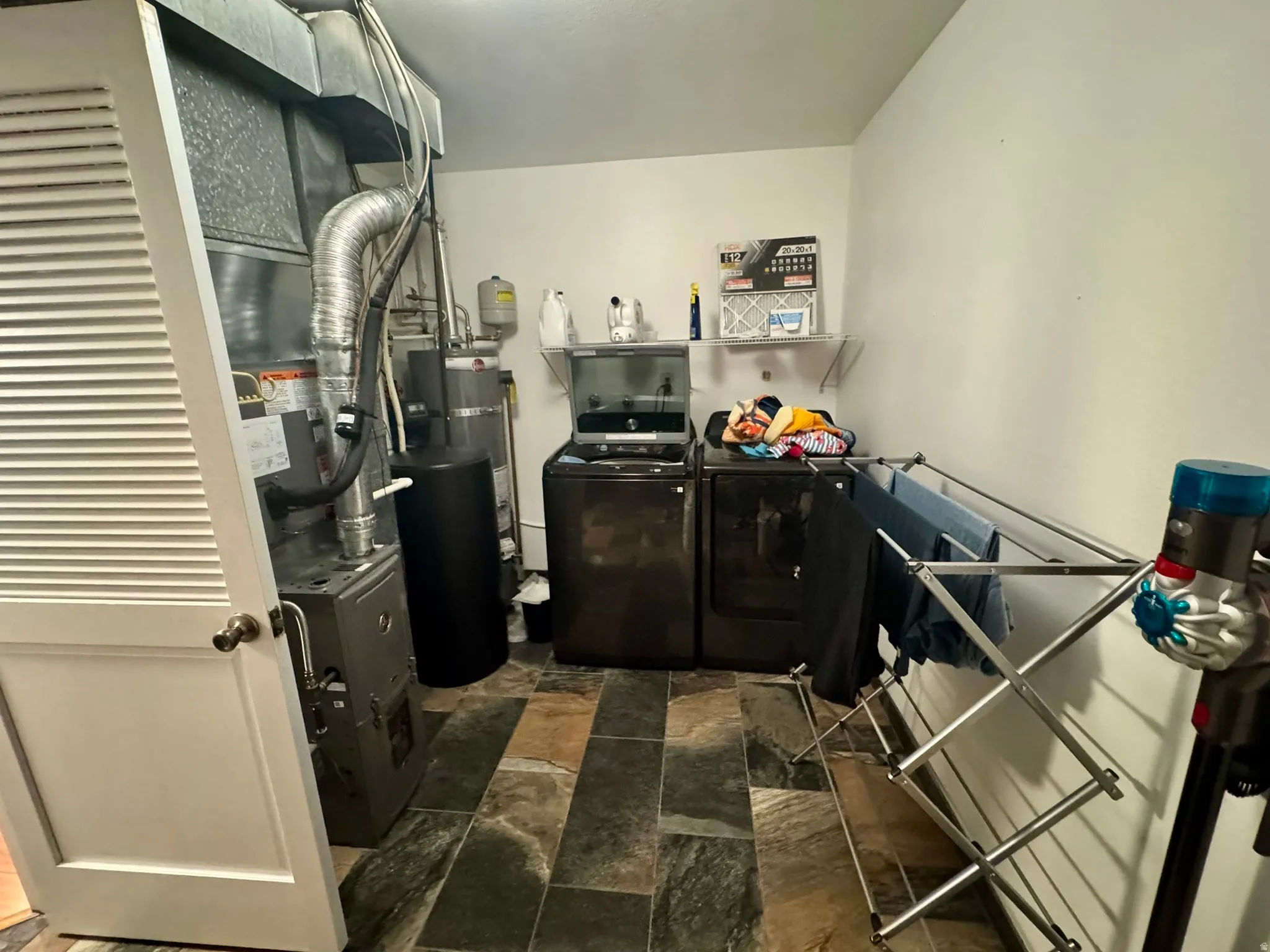 Utility space featuring a slate-tile floor, a laundry appliance pair, and a wall-mounted shelving unit