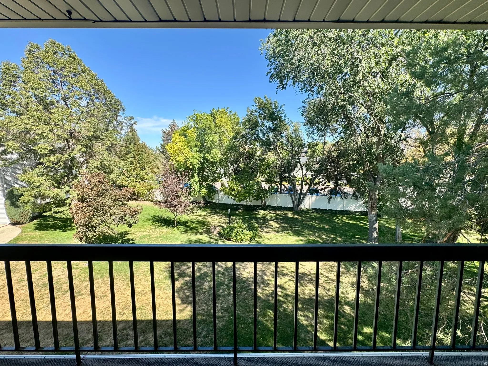 Balcony with black metal railing overlooking a landscaped area with mature trees and green space