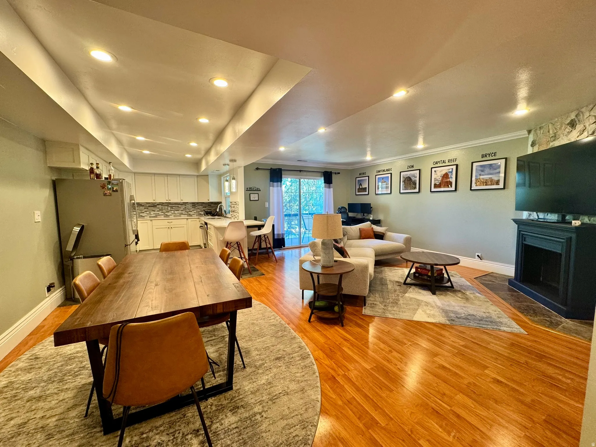 Recessed lighting throughout, wood-finish flooring, white kitchen cabinetry, mosaic tile backsplash, and a black fireplace surround with stone accent wall