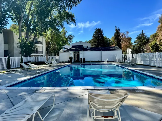 Outdoor swimming pool with a concrete deck, white perimeter fencing, and mature trees