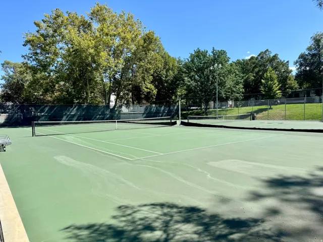 Full-size tennis court featuring a net and perimeter fencing
