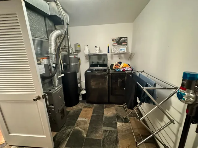 Utility space featuring a slate-tile floor, a laundry appliance pair, and a wall-mounted shelving unit