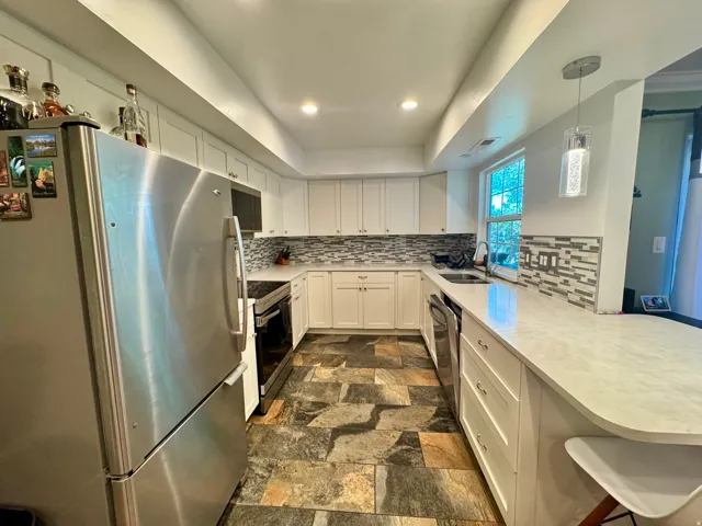Kitchen featuring crisp white cabinetry, stainless steel appliances, white countertops, a tiled backsplash, and slate-style flooring