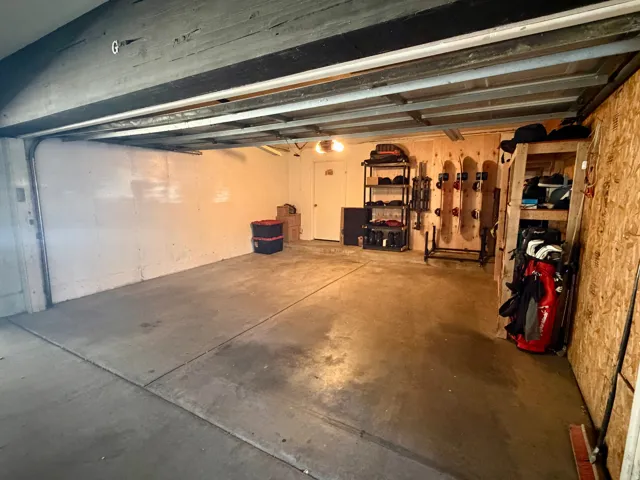Concrete flooring garage with exposed ceiling beams and a wood-paneled wall