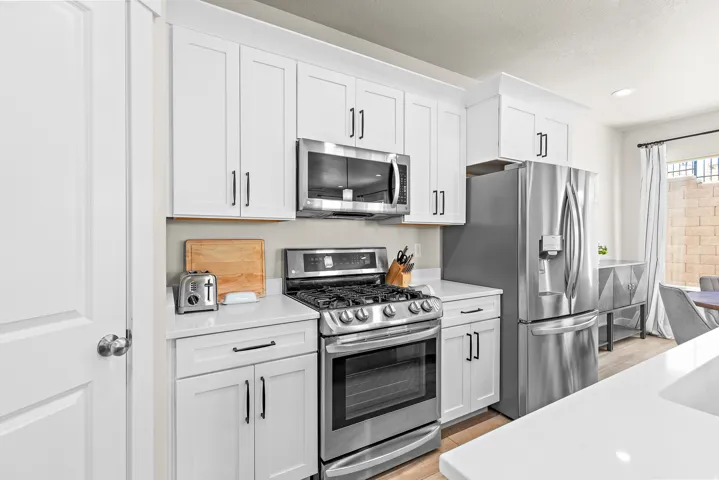 White shaker cabinetry, stainless steel appliances, quartz countertops, a gas range, and wood-finish flooring