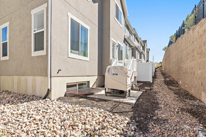 Stucco exterior with white-framed windows, concrete patio, white privacy fence, and rock landscaping