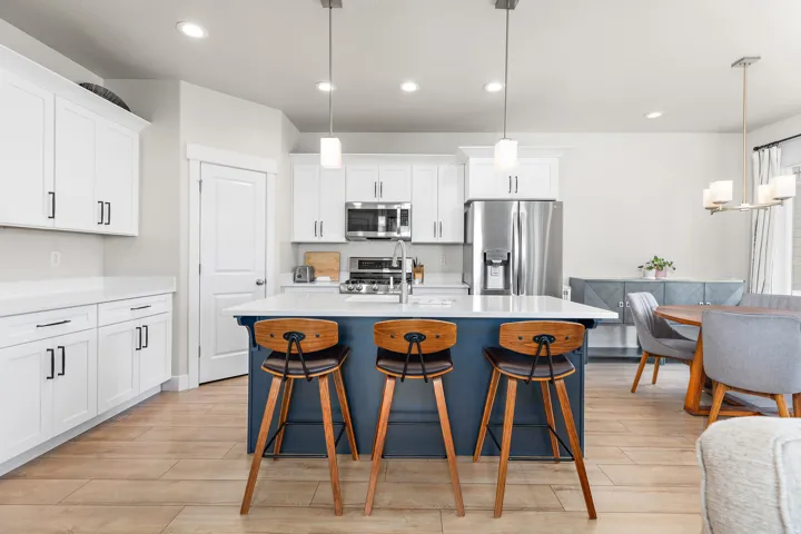 Gourmet kitchen with a blue island, white cabinetry, integrated stainless steel appliances, and wood-finish flooring