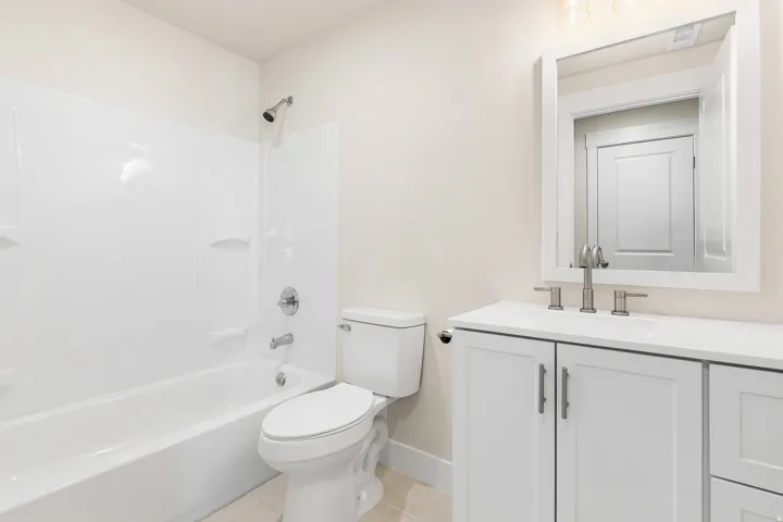 Full bathroom featuring a white tub/shower combination, white vanity with integrated sink, white framed mirror, and tile flooring