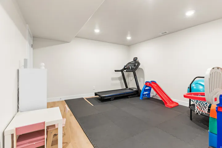 Recessed lighting illuminates a versatile finished room with light wood-finish flooring and white walls