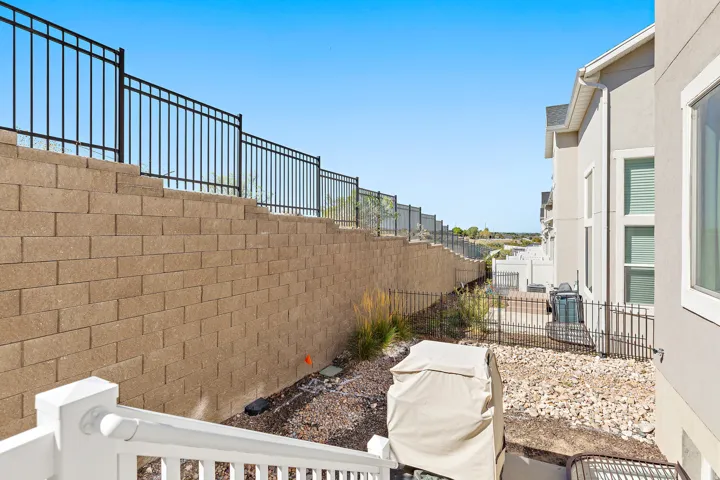 Tiered retaining wall with black metal fencing, white exterior staircase, and a gravel-covered lower yard area
