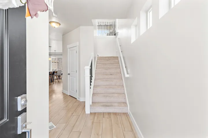 Light wood-finish flooring, staircase with carpeted treads, white painted walls, and an overhead light fixture
