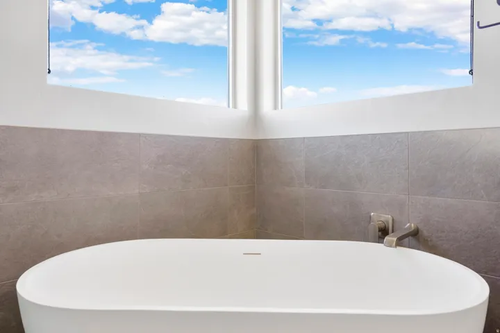 Primary bathroom - freestanding soaking tub with a modern faucet, surrounded by large format wall tile