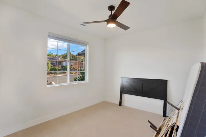 Neutral wall colors, carpet flooring, a window with grid panes, and a ceiling fan with integrated lighting