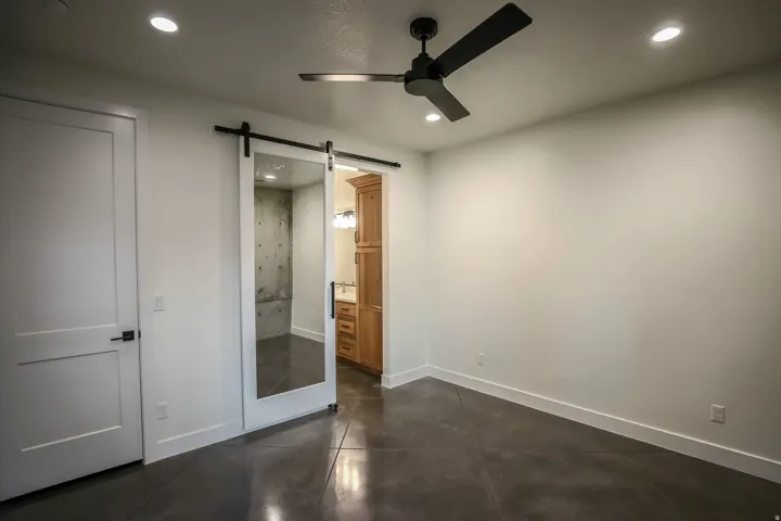 ADU - Recessed lighting, black ceiling fan, white paneled door with black hardware, mirrored barn door, polished concrete flooring