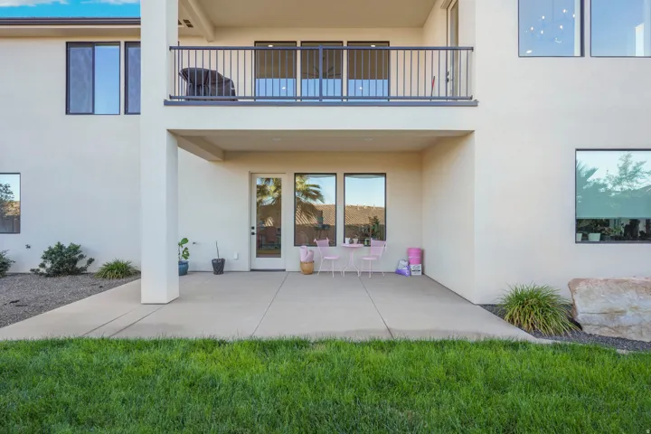 Covered patio with concrete flooring, upper-level balcony with metal railing, and expansive windows