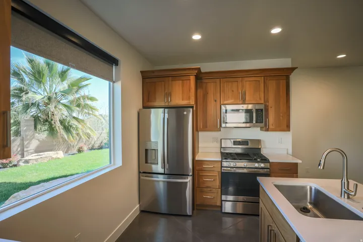 ADU - Stainless steel appliances, recessed lighting, wood-finish cabinetry, light-toned countertops, and a large window overlooking a landscaped yard
