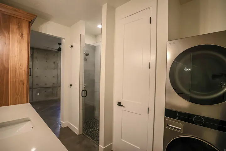 ADU - Built-in wood cabinetry, integrated sink, glass-enclosed shower with pebble floor, and stacked laundry appliances