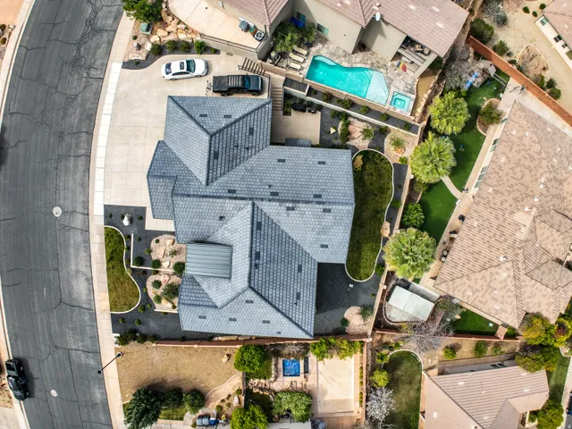 Aerial view - pitched roofline with gray shingles, concrete driveway, landscaped front yard with dark rock and greenery