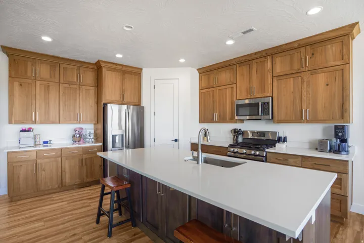 Kitchen featuring wood-finish cabinetry, stainless steel appliances, a large center island with a sink, quartz countertops, and recessed lighting