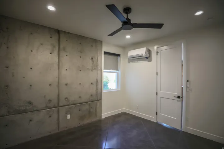 ADU - Exposed concrete accent wall, recessed lighting, matte black ceiling fan, mini-split air conditioning unit, and a two-panel interior door