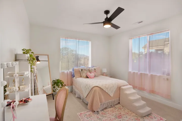 Spacious room featuring vaulted ceilings, a ceiling fan with integrated lighting, and two large windows