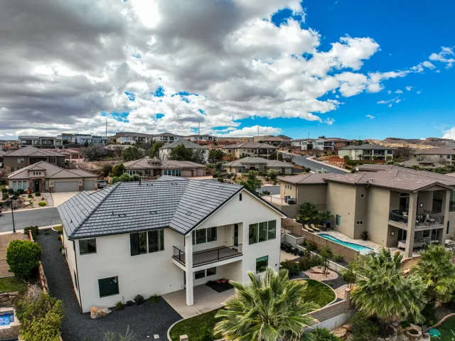 Aerial view - contemporary residence featuring a light-colored exterior, an upper-level balcony, a lower-level patio, and a dark tile roof
