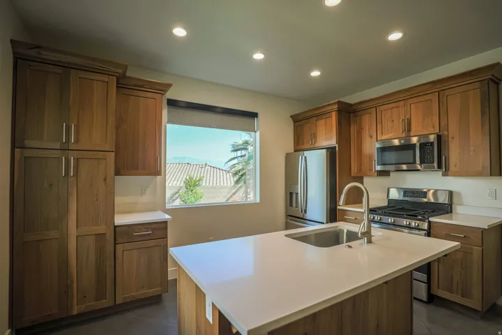 ADU - Kitchen featuring wood-finish cabinetry, stainless steel appliances, a center island with an undermount sink, recessed lighting, and light-toned countertops