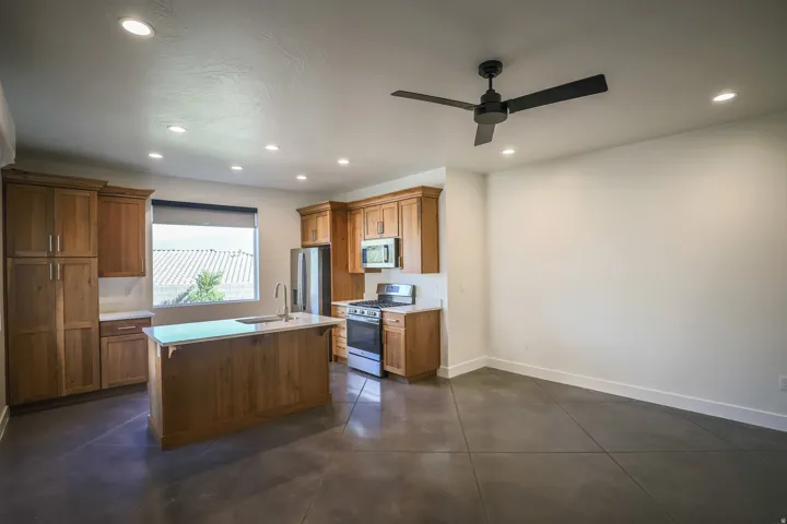 ADU - Open-concept kitchen featuring wood cabinetry, stainless steel appliances, a center island with sink, and solid surface countertops