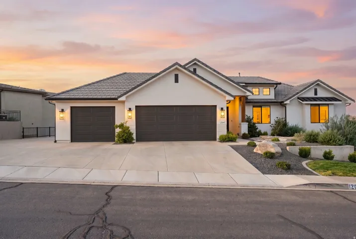 Contemporary home with a light-toned stucco exterior, dark tiled roofing, and a two-car garage