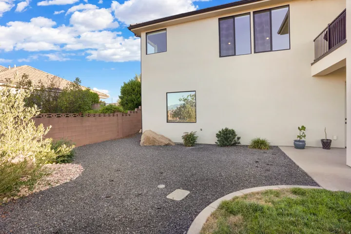 Exterior wall with multiple windows, second-story balcony with metal railing, and a ground-level patio