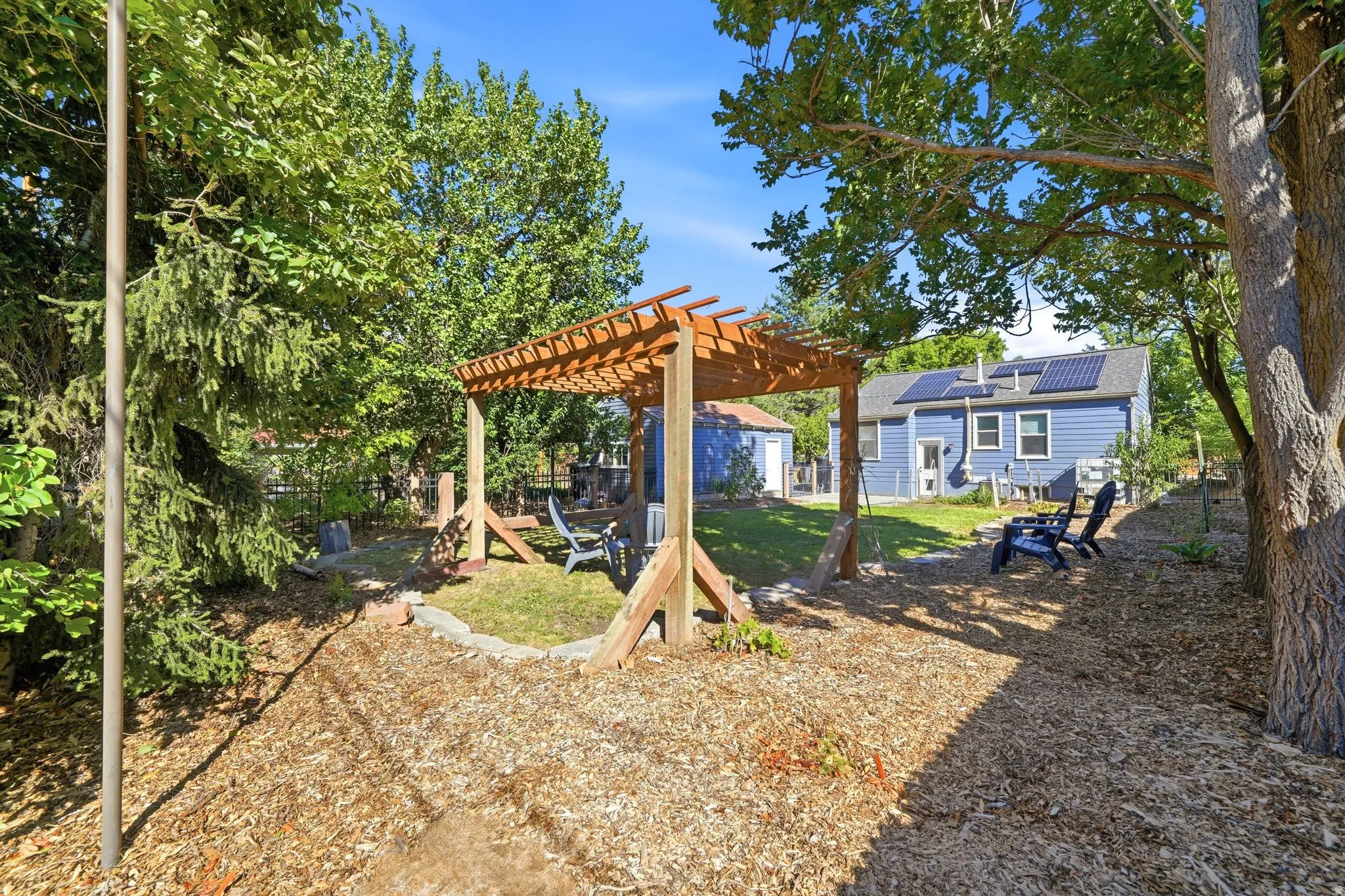 Expansive backyard featuring a wood pergola, mulched ground cover, and mature trees