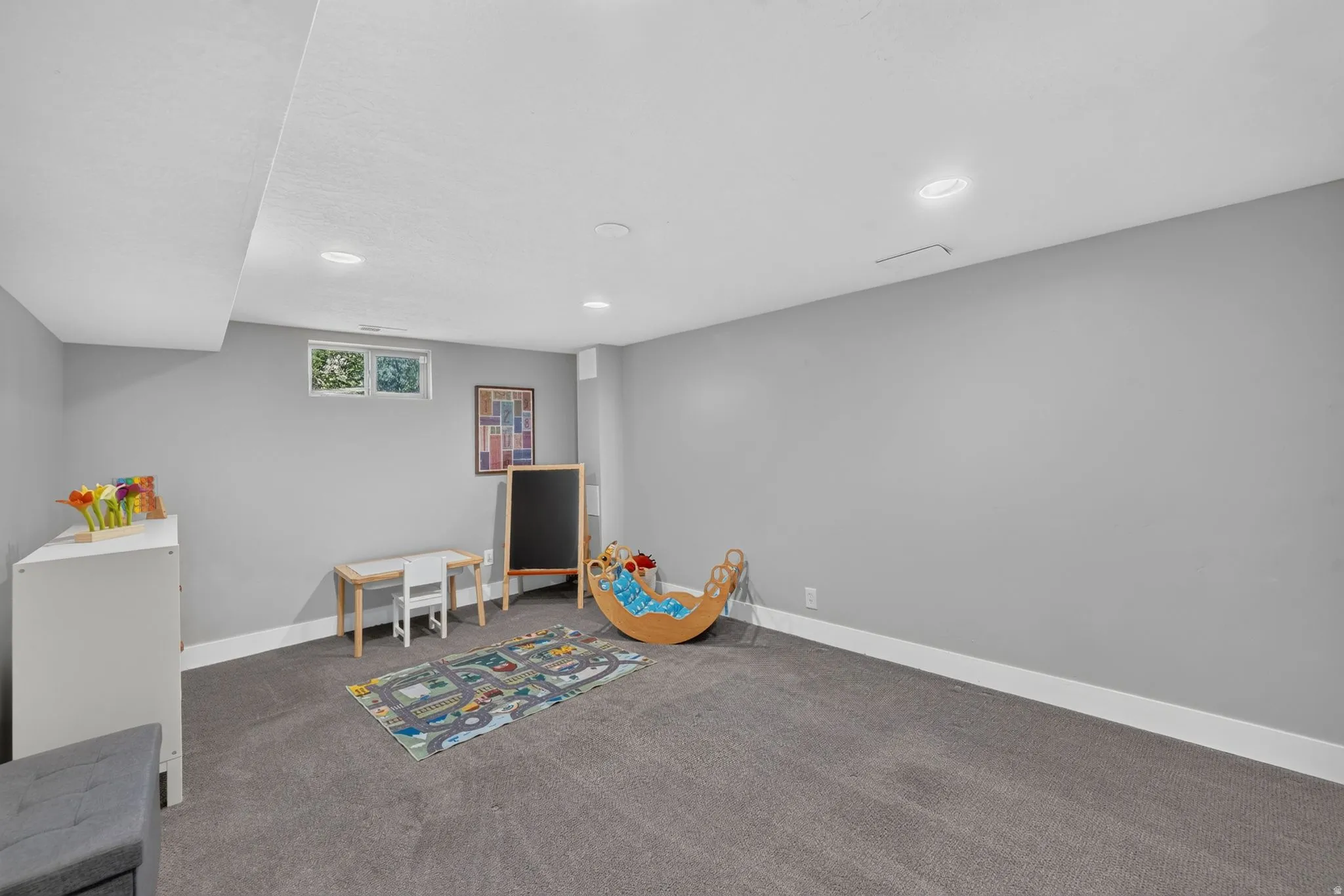 Recessed lighting illuminating the room, featuring a window with an exterior view, and dark gray carpeting