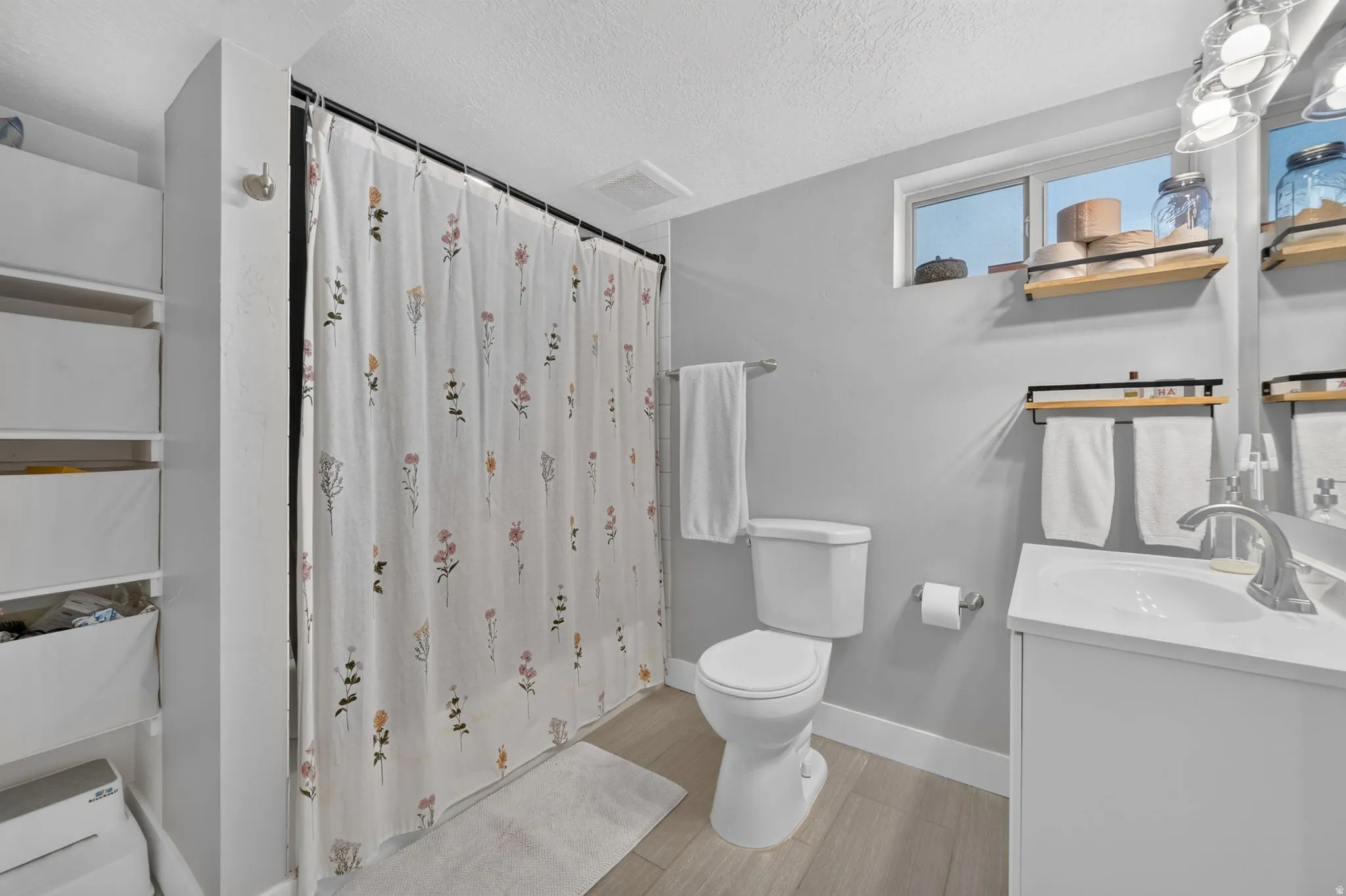 Bathroom featuring a white vanity with an integrated sink, a toilet, a shower area with a curtain rod, and light wood-finish flooring