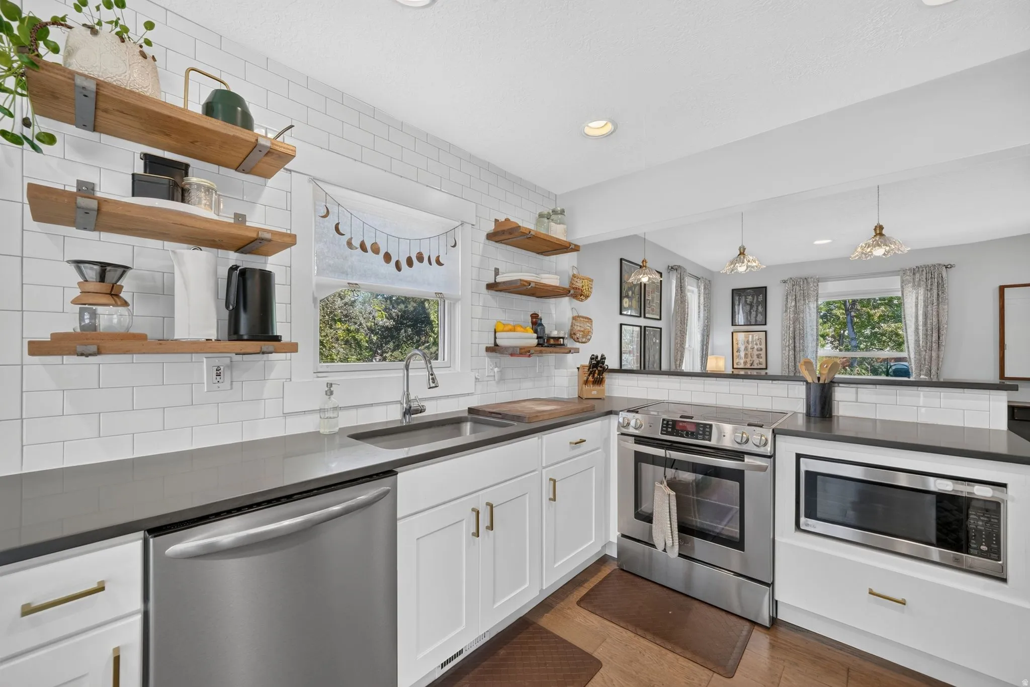 White subway tile backsplash, stainless steel appliances, dark countertops, white cabinetry with gold-finish hardware, and wood-finish flooring