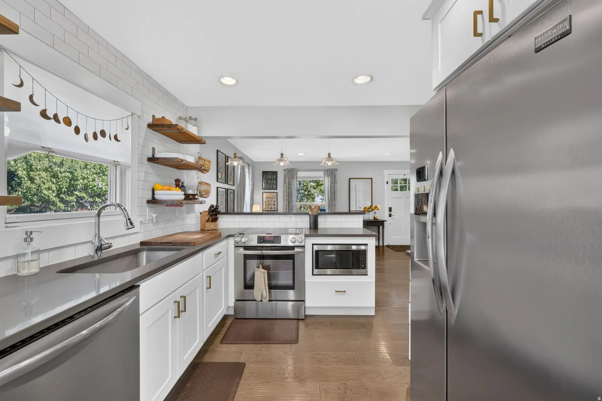 Kitchen featuring white shaker cabinetry, stainless steel appliances, dark countertops, a subway tile backsplash, and wood-finish flooring