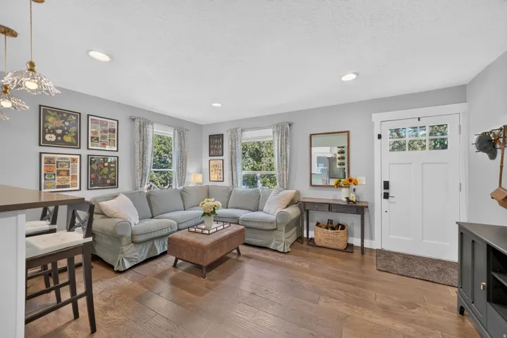 Recessed ceiling lighting, wood-finish flooring, white paneled front door with clear glass inserts, and a built-in breakfast bar