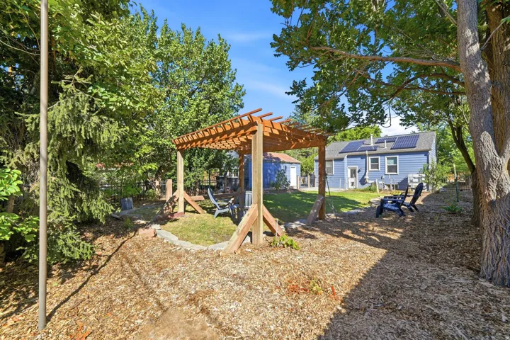 Expansive backyard featuring a wood pergola, mulched ground cover, and mature trees