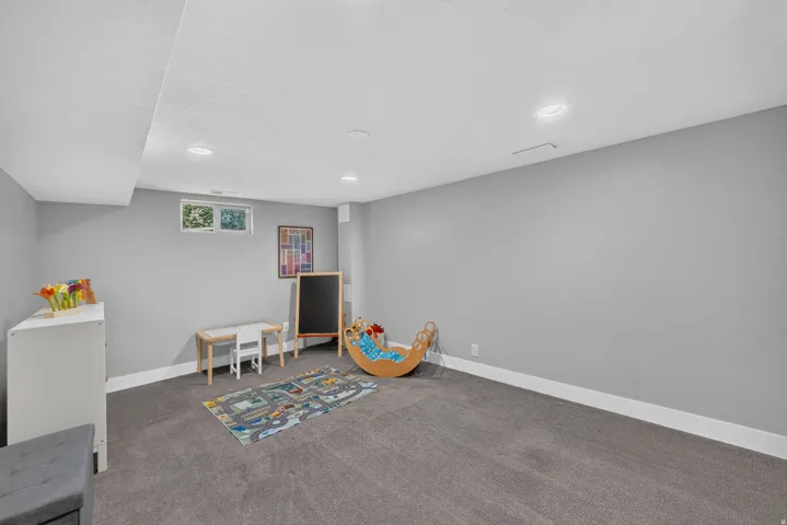 Recessed lighting illuminating the room, featuring a window with an exterior view, and dark gray carpeting