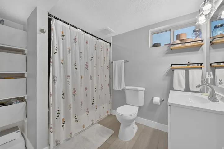 Bathroom featuring a white vanity with an integrated sink, a toilet, a shower area with a curtain rod, and light wood-finish flooring